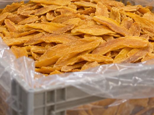 Bright orange dried mango slices filling a plastic-lined crate.